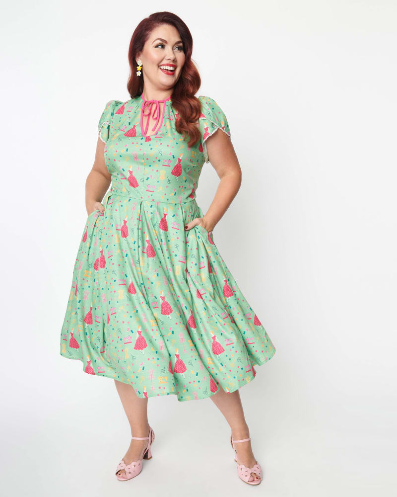 Front of a model wearing a size 5X Unique Vintage Sage & Retro Sewing Print Dahlia Swing Dress in Green by Unique Vintage. | dia_product_style_image_id:287449